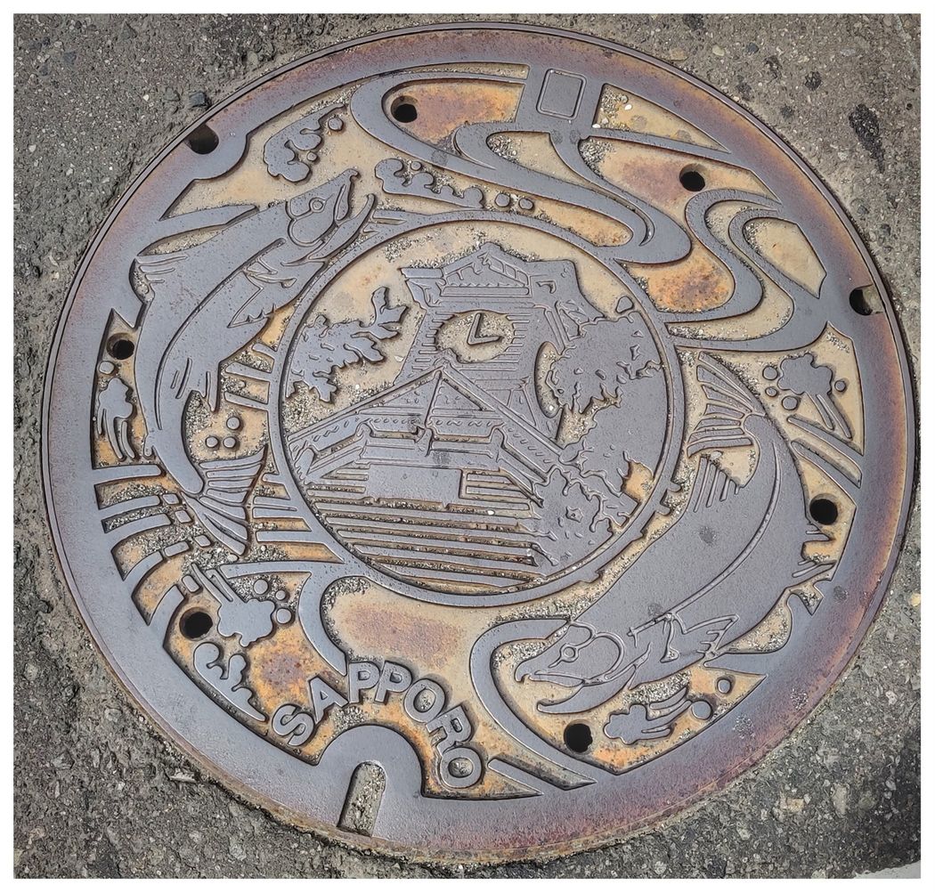 Sapporo sewer cover depicts the Sapporo Clock Tower and a pair of salmon.