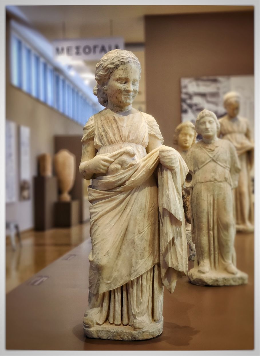 Marble statue of a girl. End of 4th century B.C. (around 320 B.C.) She is wearing a long pleated chiton, girded high under breast, and himation which is held in place by the left hand. She smiles innocently and holds a hare at the 'nest' formed by the himation.
